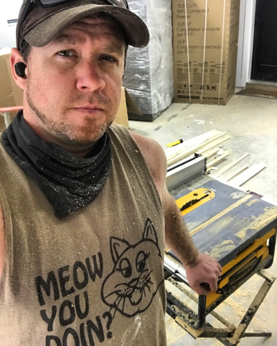 Cody Bunton on a jobsite, wearing a 'Meow You Doin?' shirt, standing next to a table saw